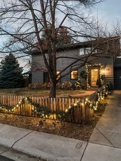 a house with christmas lights on the fence and trees in front of it, at night