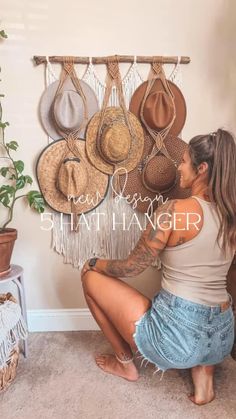 a woman sitting on the floor in front of hats hanging from a wall and holding her leg up