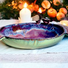 a blue and purple bowl sitting on top of a table next to a lit candle