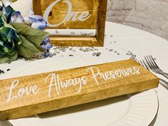 a wooden sign that says love always preservess on a table with silverware and flowers