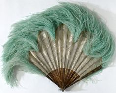 an old fan with green feathers on it's side, sitting against a white wall