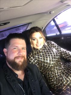 a man and woman are sitting in the back seat of a car, smiling at the camera