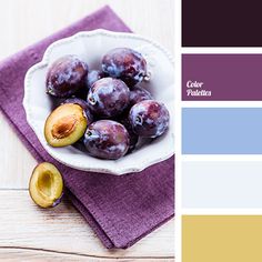 a white bowl filled with plums sitting on top of a purple cloth next to a wooden