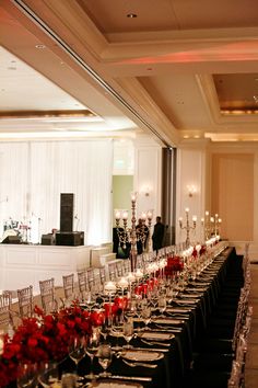 a long table is set up with red flowers and place settings for an elegant event