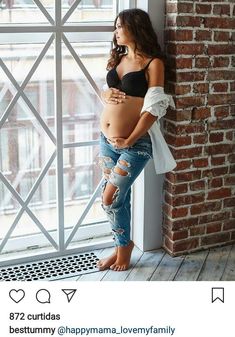 a pregnant woman leaning against a window sill in ripped jeans and a black bra