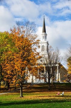 a large white church with a steeple surrounded by trees and leaves on the ground