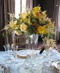 a vase filled with yellow flowers sitting on top of a table next to glasses and plates