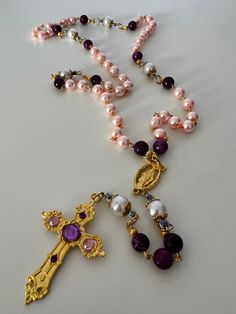 This is a beautiful gold chain link Rosary made with pretty pink and purple glass beads and white Pearl beads.  The white Pearl beads are accented with gold caps and surrounded with small amethyst beads.  Attached is a 2" gold crucifix with some added purple and pink gem embellishments.  The Virgin Mary Miraculous Medal finishes off this gorgeous Rosary.   The Rosary consists of 10 mm Our Father beads and 8 mm Hail Mary beads.  Length of the Rosary is approximately 22 1/2". This Rosary is handma Pink Beaded Amethyst Necklace, Gold Amethyst Jewelry With 8mm Beads, Gold Amethyst Beaded Necklace With Faceted Beads, Purple Pearl Jewelry With Colorful Beads, Purple Beaded Rosary As Gift, Gold Caps, Pink Gem, The Virgin Mary, The Rosary