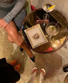 a woman sitting at a table with her legs crossed on the table and wine glasses in front of her