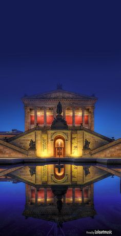 the building is lit up at night with its reflection on the water's surface