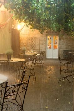 an outdoor dining area with tables and chairs under a tree in the rain at night