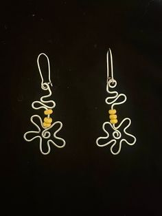 two pairs of silver and yellow earrings on a black background, one is shaped like an octopus