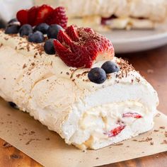 a piece of cake with berries and whipped cream on it sitting on top of a wooden table