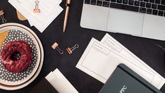 a donut sitting on top of a plate next to a laptop computer and papers