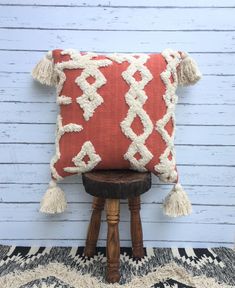 an orange and white pillow with tassels on it sitting on a wooden stool