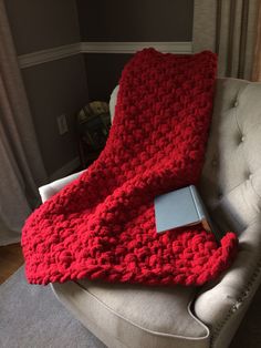 a red crocheted blanket sitting on top of a couch next to a laptop computer