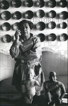 an old woman standing in front of a sculpture holding a cell phone to her ear