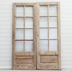 an old pair of double doors against a white brick wall with wood trim and glass panes