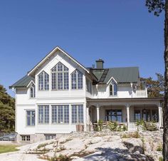 a large white house sitting on top of a rock covered hillside next to a forest