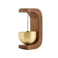 a golden bowl on a wooden shelf with a metal object hanging from it's side