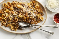 a plate full of pasta with meat and cheese on it next to two bowls of sauce