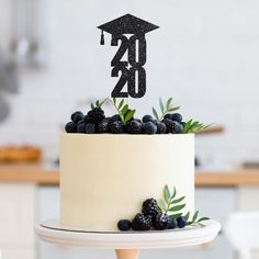 a white cake topped with berries and a black graduation hat topper sitting on a table