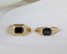 two gold rings with black stones sitting on top of each other in front of a white cloth