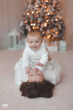 a woman holding a baby in front of a christmas tree