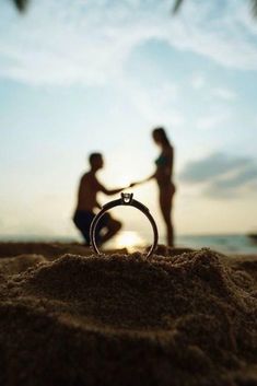 two people standing on the beach with a ring in their hand and one person sitting down