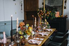 a long table with candles and flowers on it in front of a mirror that is next to a fireplace