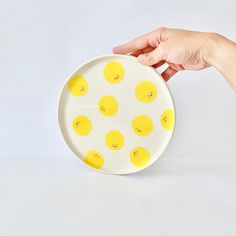 a hand is holding a yellow and white plate with smiley faces on it, against a white background