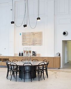 an empty room with several chairs and a table in the center, surrounded by white walls