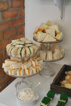 a table topped with lots of different types of sandwiches and desserts next to a brick wall