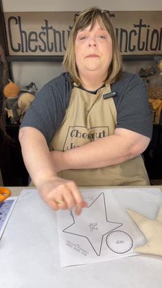 a woman sitting at a table with an apron on and pointing to the star cut out