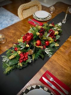 the table is set with red and green flowers, pine cones, greenery, silverware