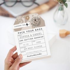 a person holding up a ticket for their wedding day with flowers in the vase behind them