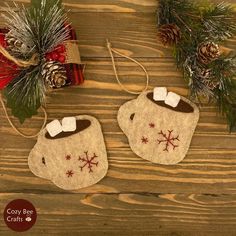 two felt christmas mitts with bows and snowflakes hanging from them on a wooden table