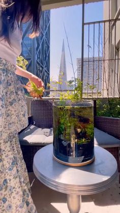 a woman standing next to a fish tank filled with plants on top of a table