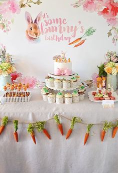 a table with carrots and cupcakes on it in front of a bunny banner