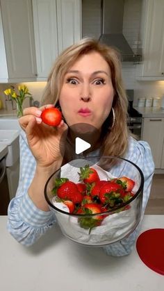 a woman holding a bowl full of strawberries in front of her face and making a funny face