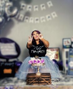 a woman in a black shirt and blue skirt is holding her hands up while sitting on top of a cake