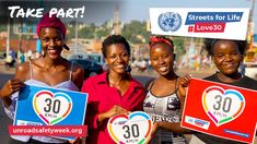 three women holding up signs with the number 30 on them in front of a city street