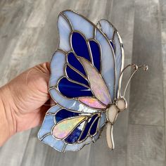 a hand holding a stained glass butterfly brooch in it's left side, on a wooden floor