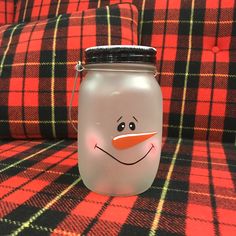 a glass jar with a snowman face on it sitting on a plaid fabric couch