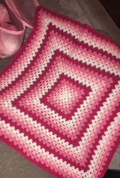 a pink and white crocheted blanket sitting on top of a floor next to a bag