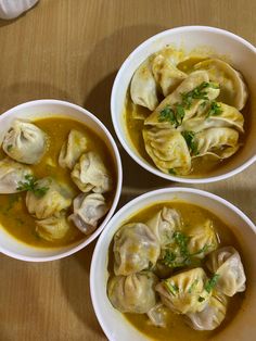 three white bowls filled with soup and dumplings on top of a wooden table,