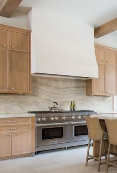 a kitchen with wooden cabinets and stainless steel stove top oven, island table and stools