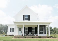 a white house with black shutters and two children sitting on the front porch outside