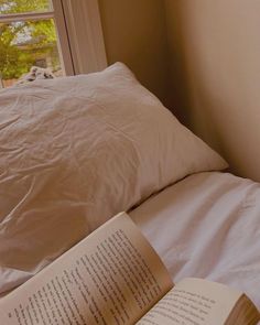 an open book sitting on top of a bed next to pillows and a pillow case