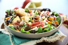 a white bowl filled with salad sitting on top of a wooden table next to an apple